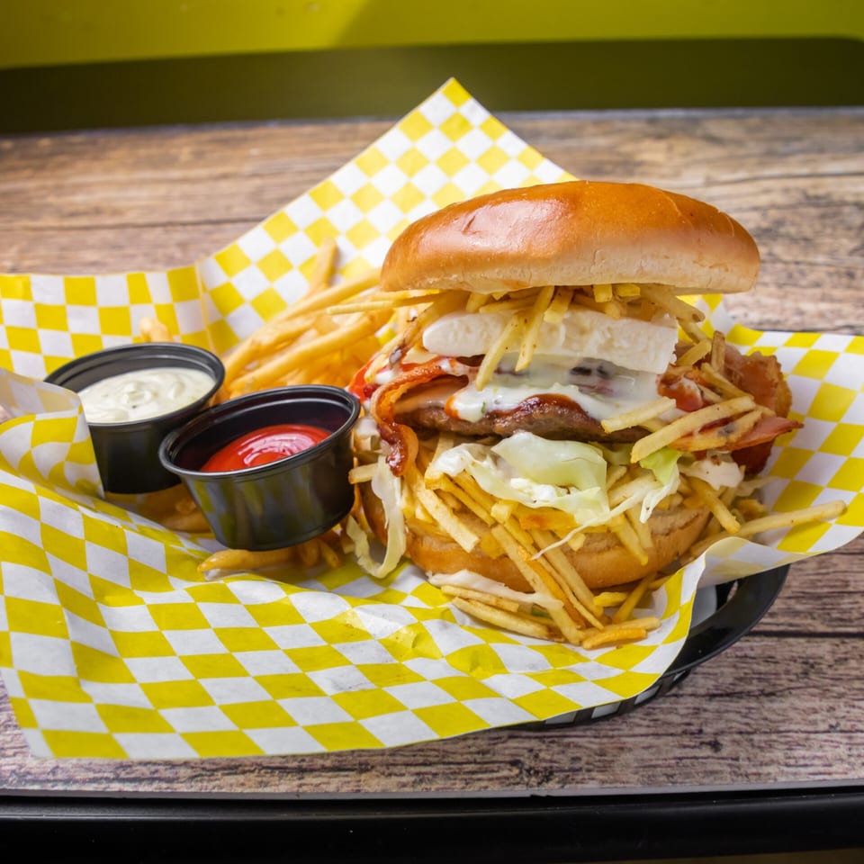 A Venezuelan burger with white cheese, bacon, shredded lettuce, and potato sticks, served with fries and sauces.