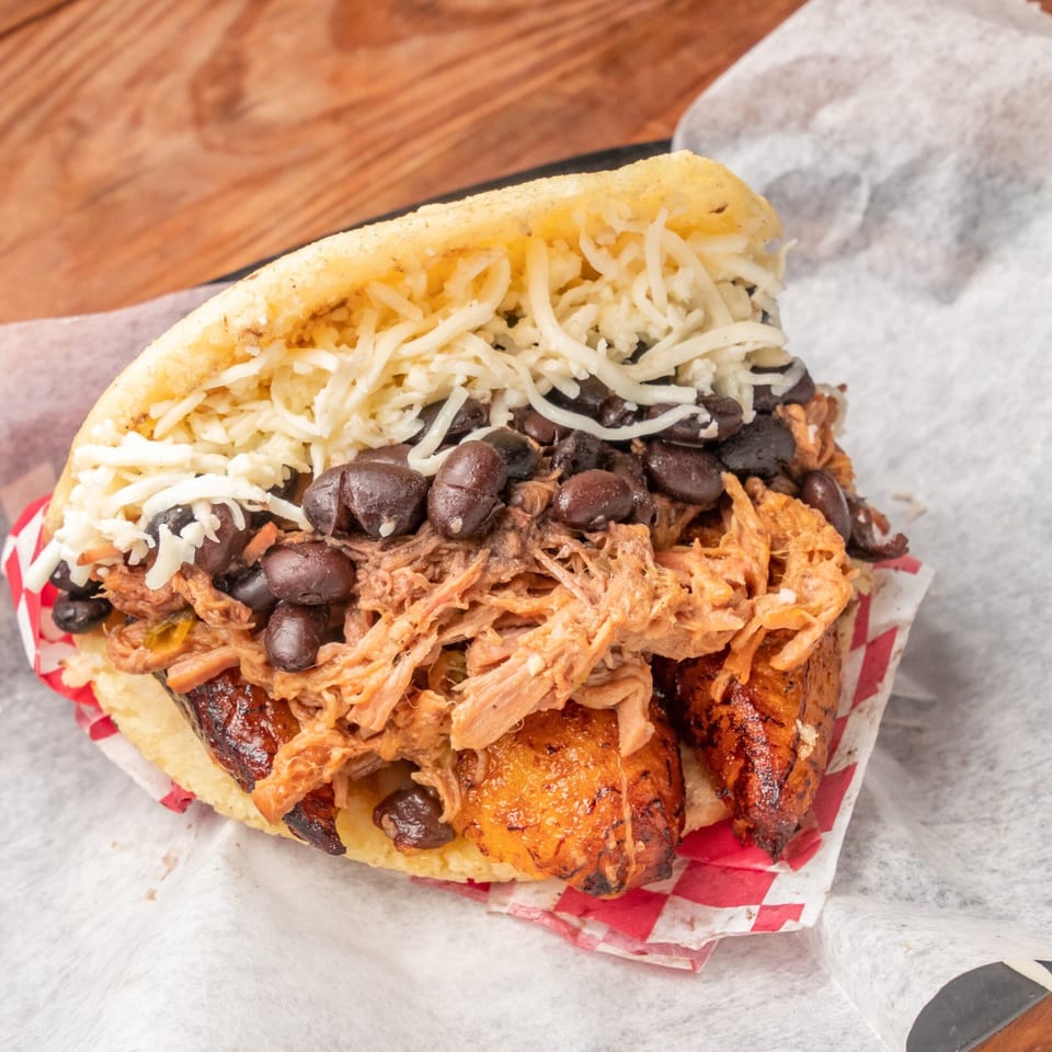 Close-up of a Venezuelan arepa filled with shredded meat, black beans, fried plantains, and cheese.
