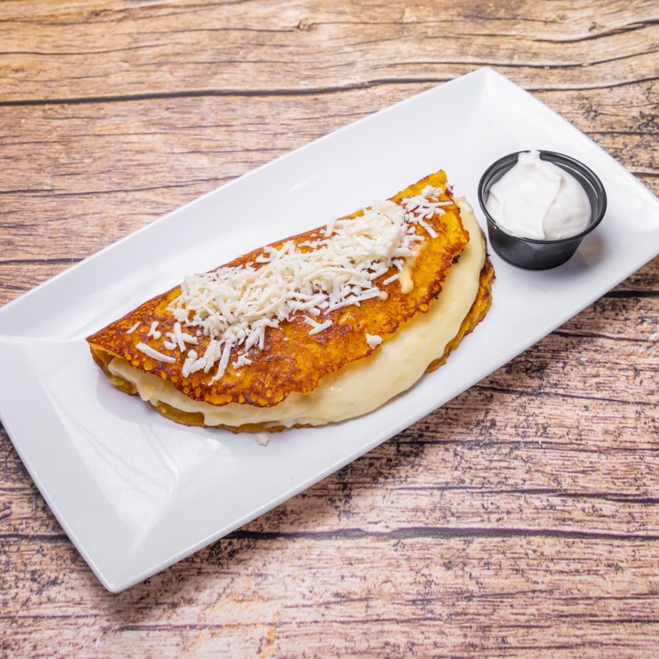 Venezuelan cachapa with cheese and a side of nata on a white rectangular plate.