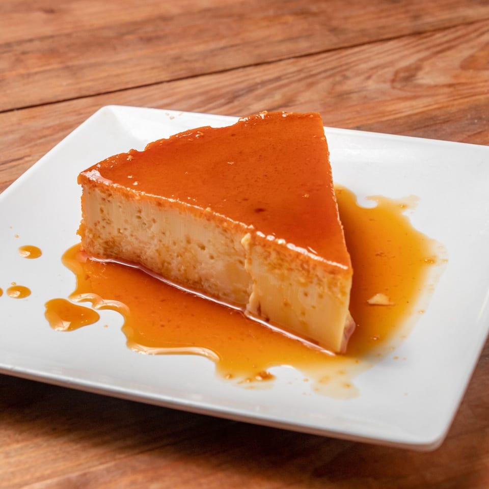 A slice of Venezuelan flan with caramel sauce on a white rectangular plate.
