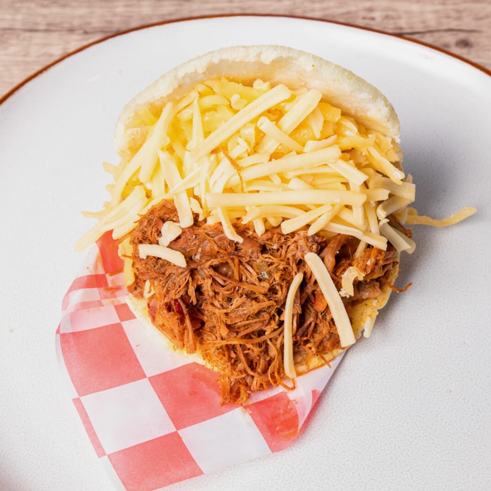 Close-up of a Venezuelan arepa filled with shredded beef and generous amounts of shredded white cheese.