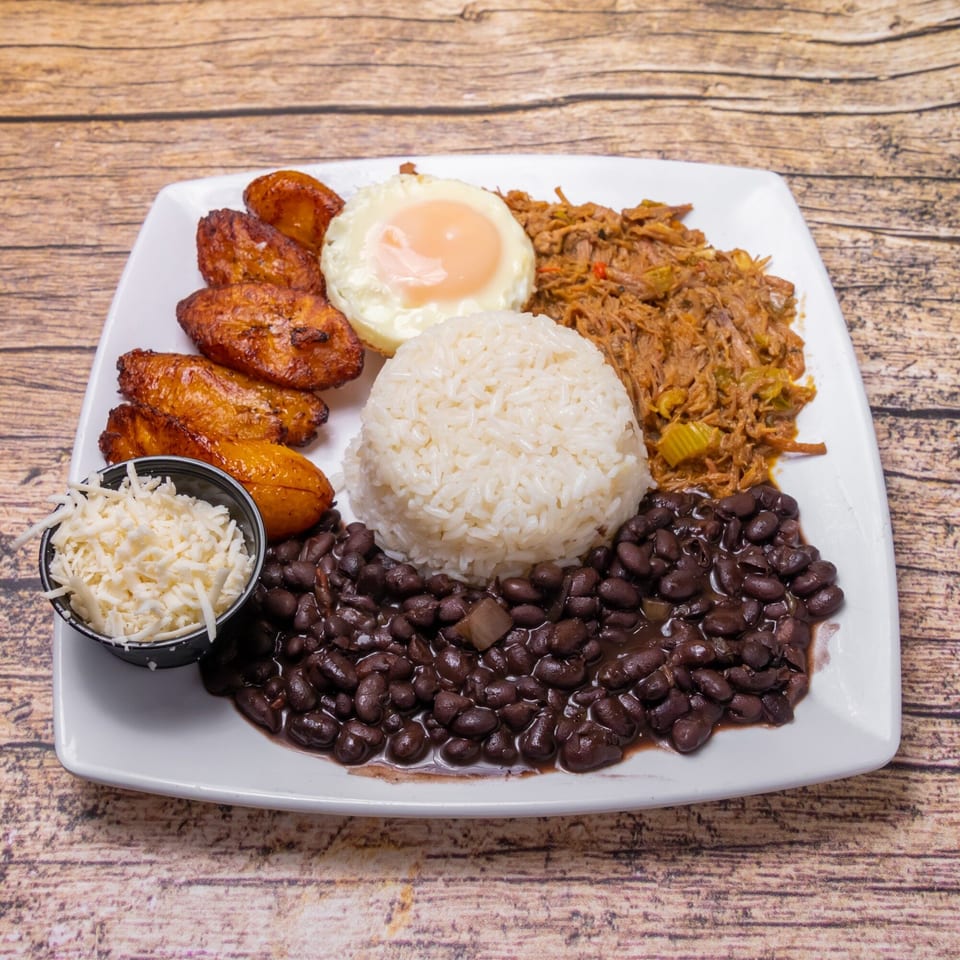 Venezuelan pabellón criollo with shredded beef, rice, black beans, fried plantains, and a fried egg.