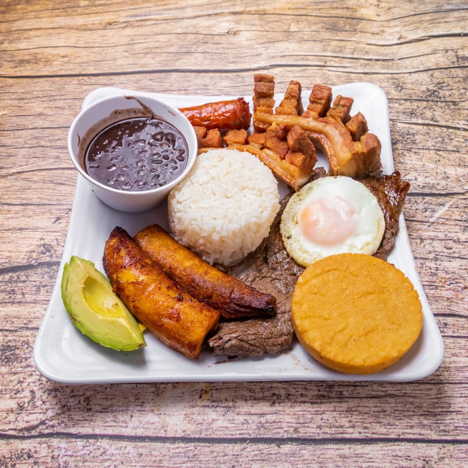 Venezuelan platter with black beans, rice, fried plantains, avocado, steak, fried egg, and pork.