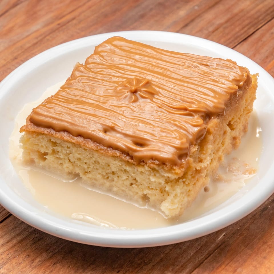 A slice of Venezuelan tres leches cake with dulce de leche frosting on a white plate.