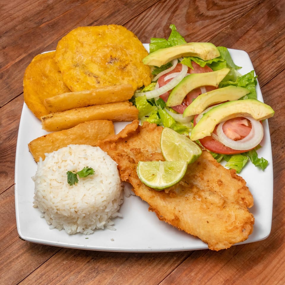 Venezuelan fried fish with rice, plantains, yuca fries, and a fresh salad with avocado and lime.