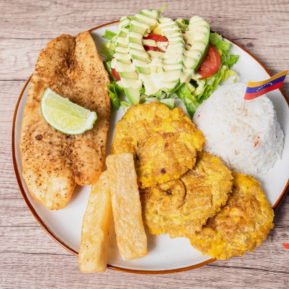 Venezuelan dish with fried fish, plantains, yucca fries, rice, and avocado salad, garnished with a flag.