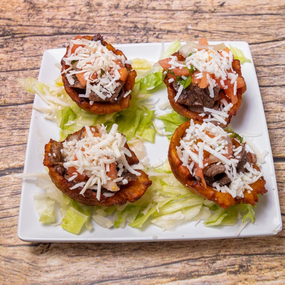 Four Venezuelan tostones, filled with beef, diced tomatoes, and shredded cheese, on a bed of lettuce.
