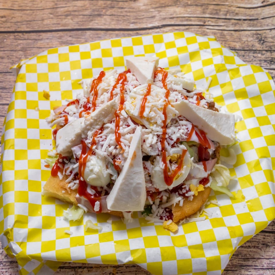 Venezuelan patacon with shredded cheese, sliced boiled eggs, and ketchup on yellow checkered paper.