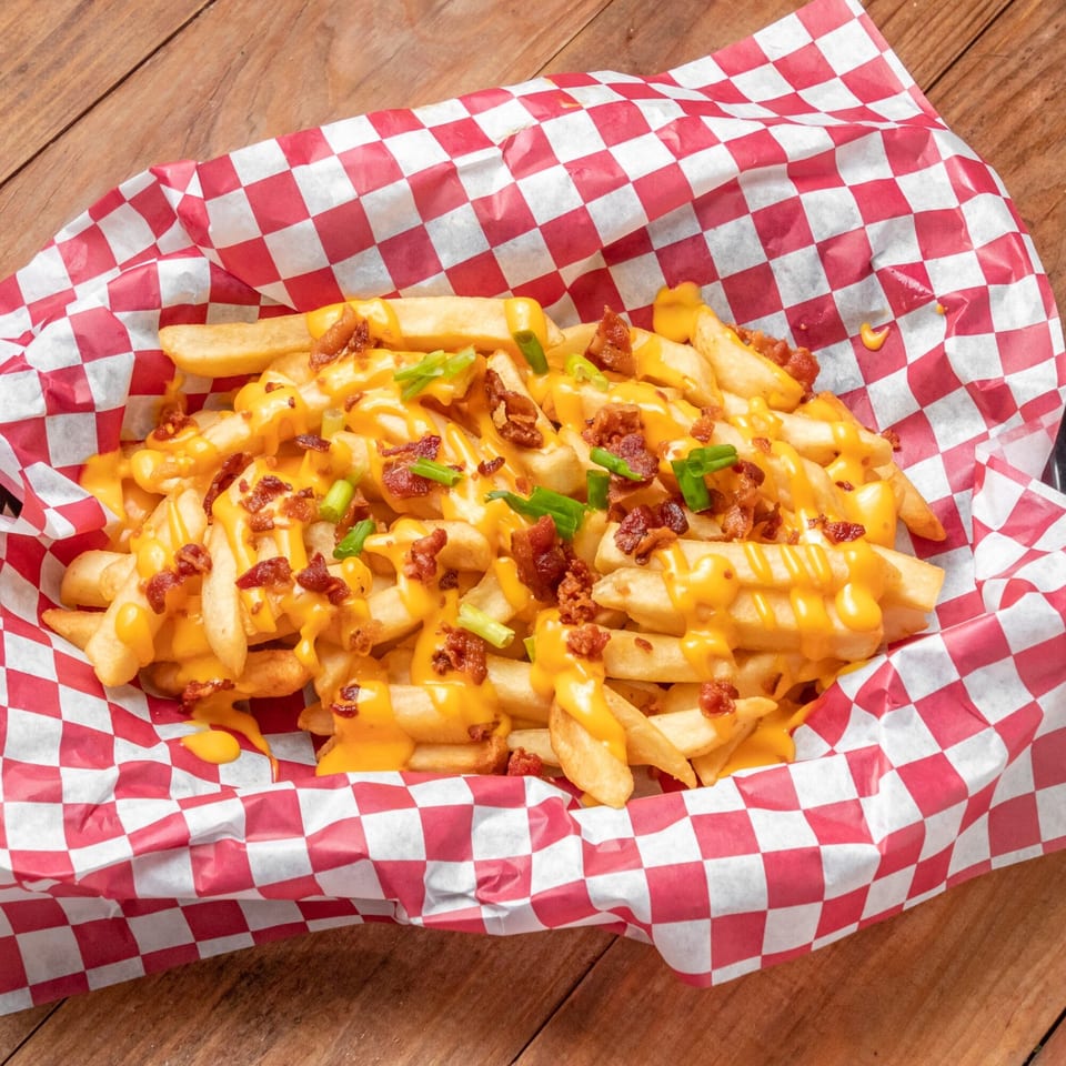 Loaded fries with melted cheese, bacon bits, and green onions in a red and white checkered basket.