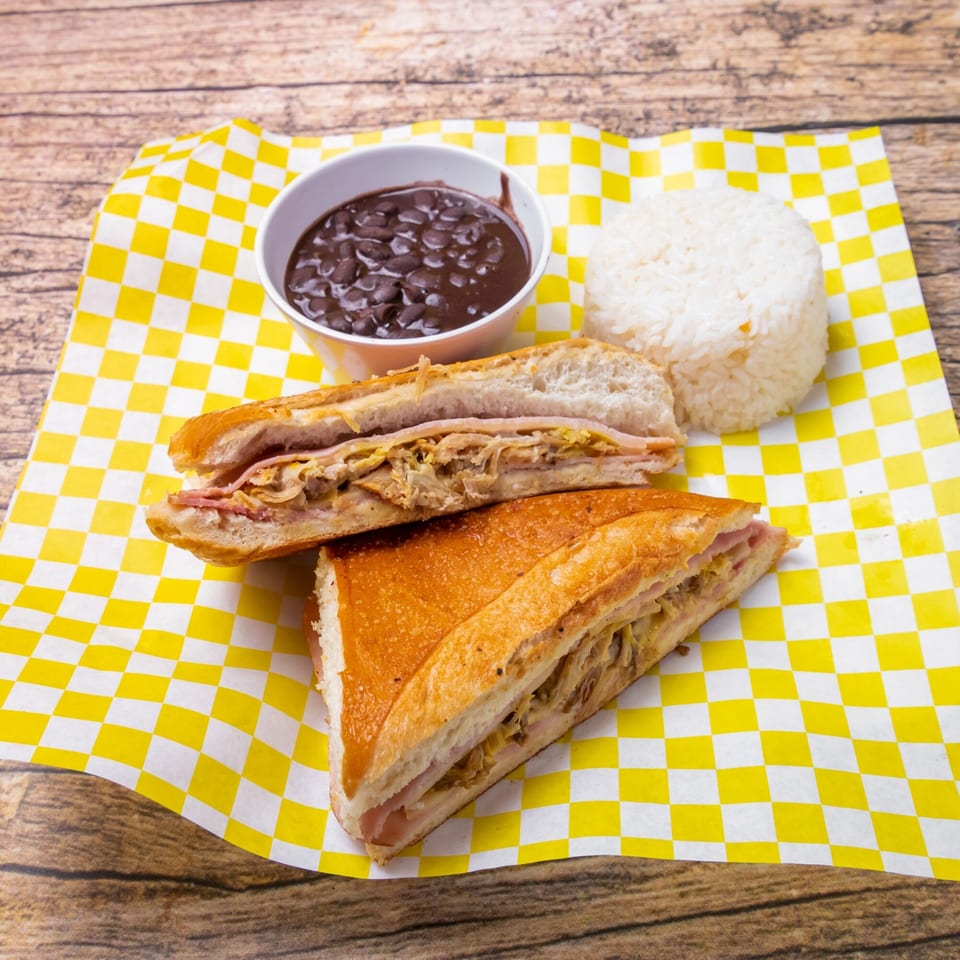 Venezuelan Cuban sandwich with black beans and white rice on yellow checkered paper.
