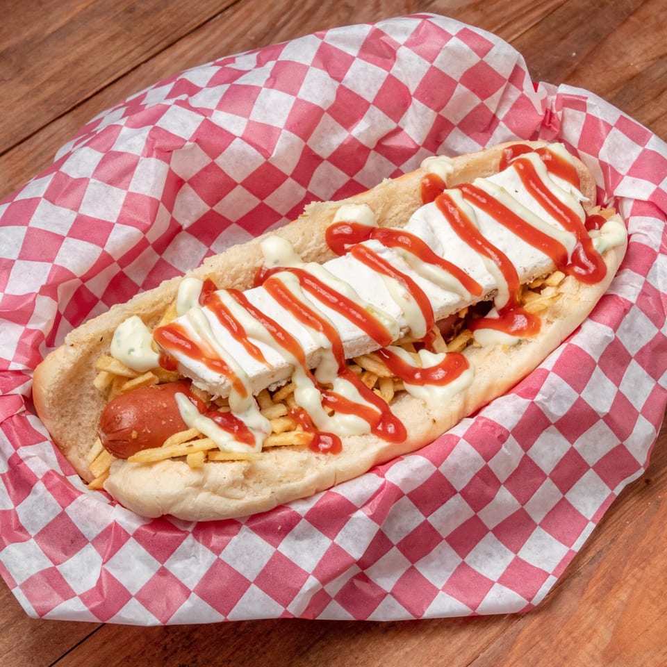 Venezuelan hot dog with sausage, cheese, potato sticks, ketchup, and mayonnaise in a red checkered wrapper.