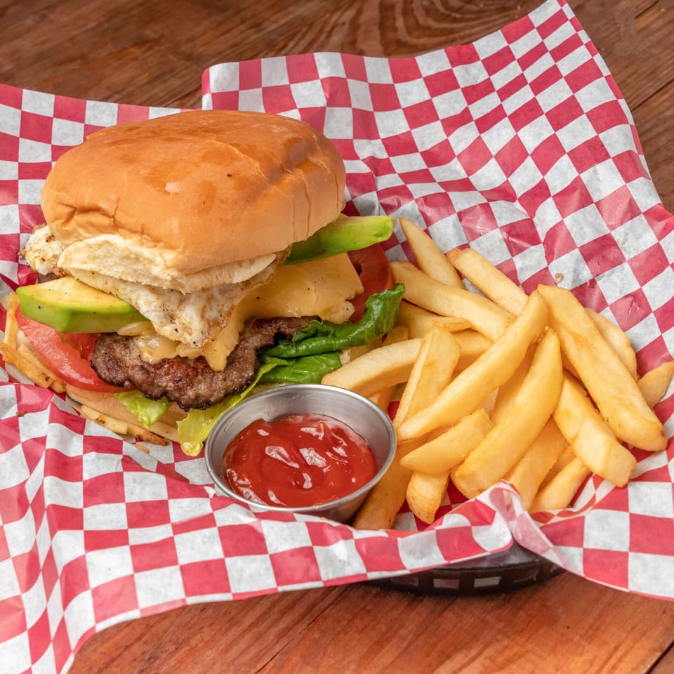 A Venezuelan burger with avocado, fried egg, cheese, lettuce, and tomato, served with fries and ketchup.