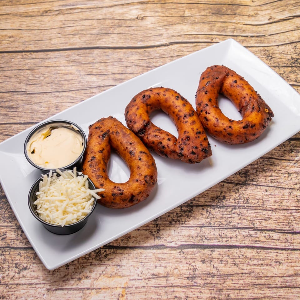 Three golden-brown Venezuelan mandocas, with two small bowls of white cheese and creamy sauce on a white plate.