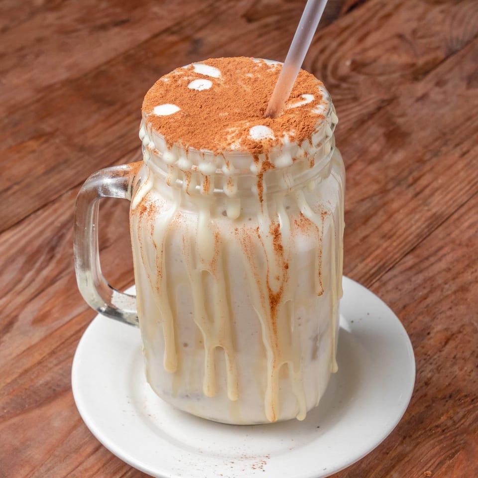 Venezuelan chicha drink in a mason jar, topped with cinnamon and a straw, on a wooden table.