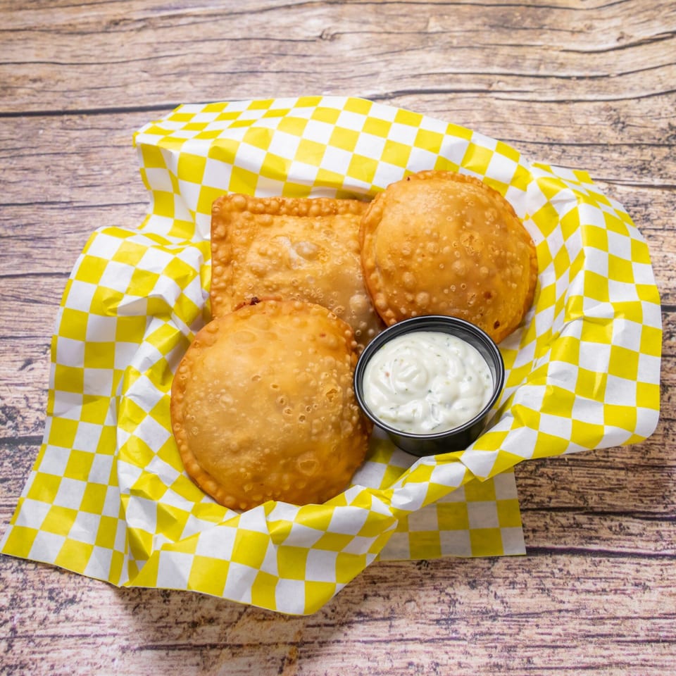 Three golden-fried Venezuelan empanadas in a yellow and white checkered paper basket with dipping sauce.